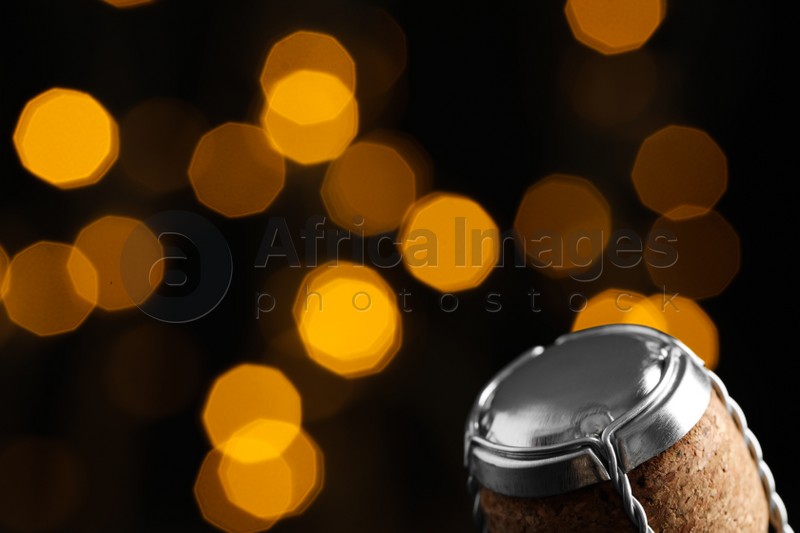 Sparkling wine cork with muselet cap against blurred festive lights, closeup. Space for text