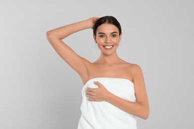 Young woman showing hairless armpit after epilation procedure on light grey background
