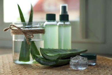 Green aloe vera leaves and cosmetic products on table near window indoors