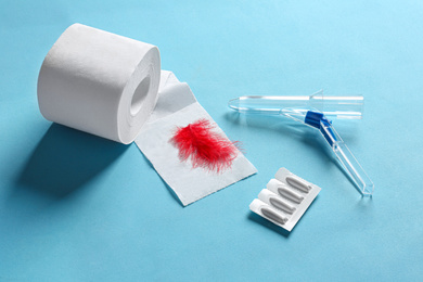 Anoscope, suppositories and toilet paper with red feather on light blue background. Hemorrhoid treatment