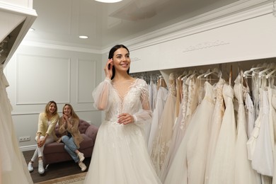 Photo of Bride with friends choosing wedding dress in boutique