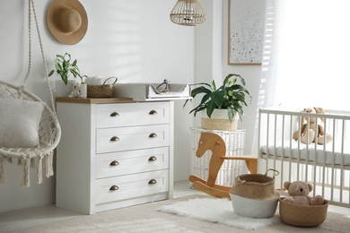 Chest of drawers with changing tray and pad near comfortable cradle in baby room. Interior design