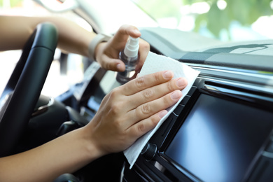 Woman cleaning dashboard with wet wipe and antibacterial spray in car, closeup