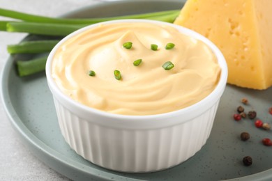 Tasty cheese sauce with green onion and peppercorns on light grey table, closeup