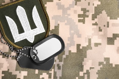 Military patch and ID tags on pixel Ukrainian camouflage, flat lay. Space for text