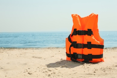 Orange life jacket on sandy beach near sea. Emergency rescue equipment