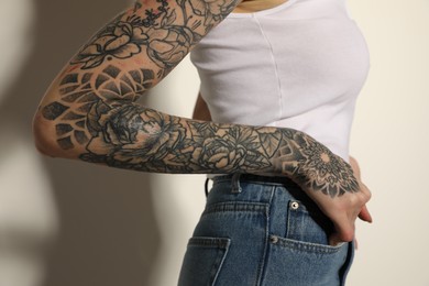 Woman with tattoos on arm against light background, closeup