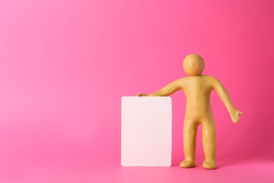 Human figure made of yellow plasticine holding blank sign on pink background. Space for text