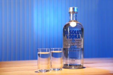 Photo of MYKOLAIV, UKRAINE - SEPTEMBER 23, 2019: Absolut vodka and shot glasses on wooden bar counter. Space for text