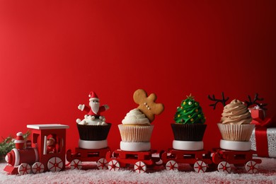 Toy train with tasty Christmas cupcakes on red background