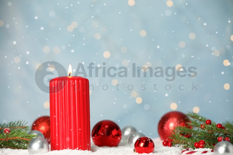 Photo of Snow falling on burning candle and festive decor against light blue background with blurred lights, space for text. Christmas eve