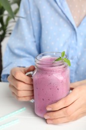 Woman with mason jar of delicious blackberry smoothie at white table indoors, closeup