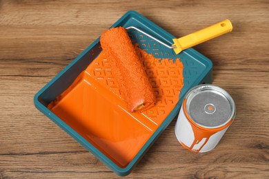 Photo of Can of orange paint, tray and roller on wooden table