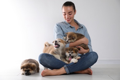 Photo of Woman with Akita Inu puppies sitting on floor near light wall