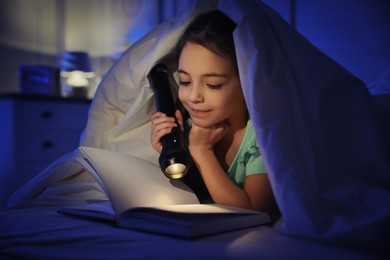 Little girl with flashlight reading fairy tale in dark bedroom