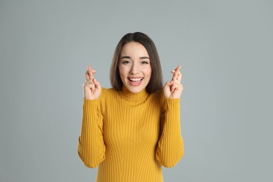 Excited young woman holding fingers crossed on grey background. Superstition for good luck