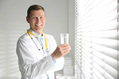 Nutritionist with glass of water near window in office. Space for text