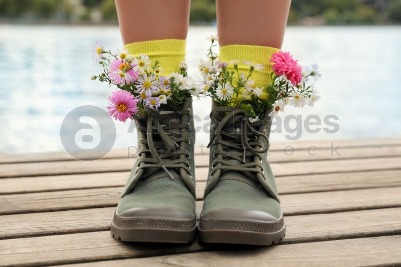 Woman with beautiful tender flowers in socks on wooden pier, closeup