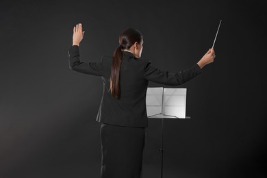 Photo of Professional conductor with baton and note stand on dark background, back view