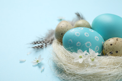Colorful Easter eggs in decorative nest on light blue background, closeup. Space for text