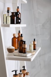 Essential oils, sea salt, and other cosmetic products on white shelving unit in bathroom