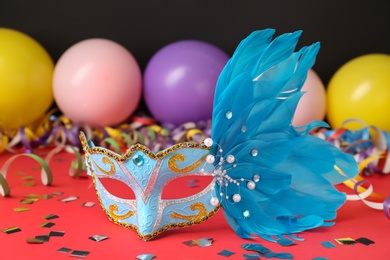 Beautiful carnival mask and party decor on red table, closeup