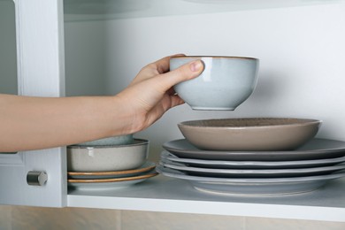 Photo of Woman taking ceramic bowl from cabinet at home, closeup
