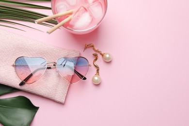 Heart shaped sunglasses with bag, earrings and glass of drink on pink background, flat lay. Space for text