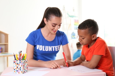 Photo of Little African-American boy learning alphabet with volunteer at table indoors