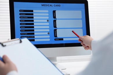 Photo of Doctor using computer to fill out patient's medical card at table in clinic, closeup