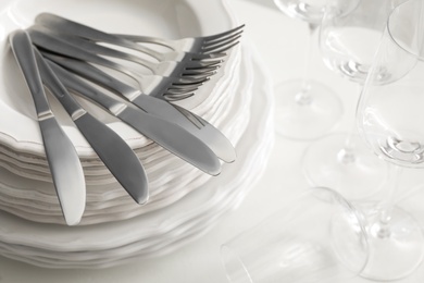 Stacked plates with cutlery and glasses on white table, closeup