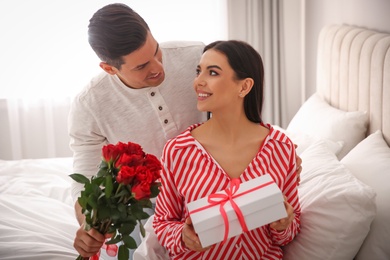 Man presenting gift and bouquet to his beloved woman at home. Valentine's day celebration