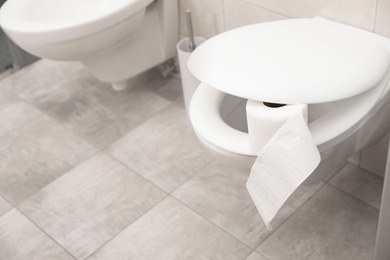 Toilet bowl with paper roll in bathroom. Space for text