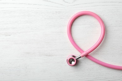 Pink stethoscope folded like awareness ribbon on wooden background, top view with space for text. Breast cancer concept