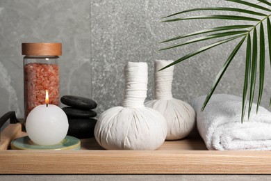 Photo of Herbal massage bags, spa stones, sea salt, rolled towel and candle on grey table