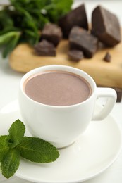 Cup of delicious hot chocolate and fresh mint on white wooden table, closeup