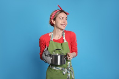 Photo of Young housewife with pot on light blue background