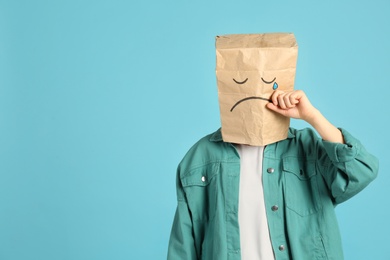Woman wearing paper bag with drawn sad face on light blue background. Space for text