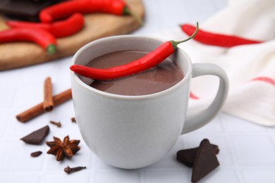 Photo of Cup of hot chocolate with chili pepper on white tiled table