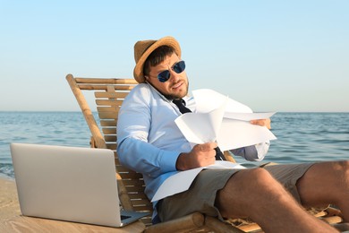 Photo of Busy man with papers talking by mobile phone on beach. Business trip