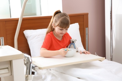 Little child with intravenous drip eating soup in hospital bed