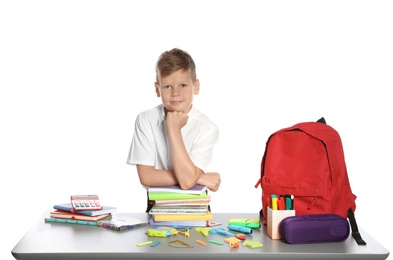 Photo of Cute boy sitting at table with school stationery against white background