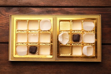 Photo of Partially empty box of chocolate candies on wooden table, top view
