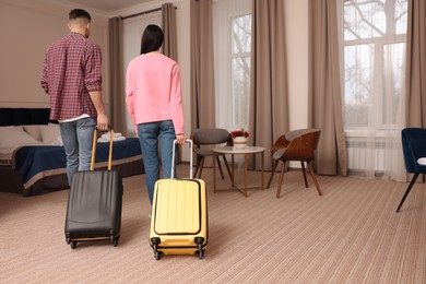 Couple with suitcases walking into hotel room, back view
