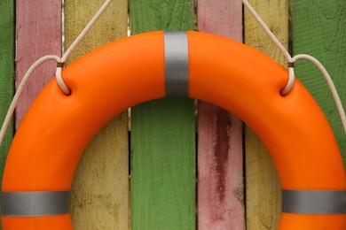 Orange lifebuoy hanging on color wooden fence, closeup. Rescue equipment
