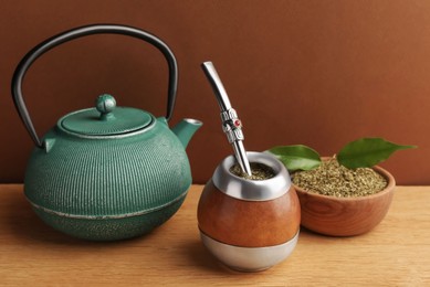 Calabash with mate tea, bombilla and teapot on wooden table
