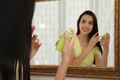 Woman applying dry shampoo onto her hair near mirror, closeup
