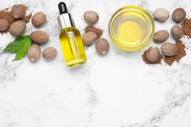 Photo of Bottle and bowl of nutmeg oil, nuts on white marble table, flat lay. Space for text