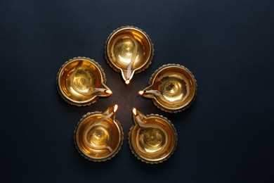 Photo of Lit diyas on dark background, flat lay. Diwali lamps