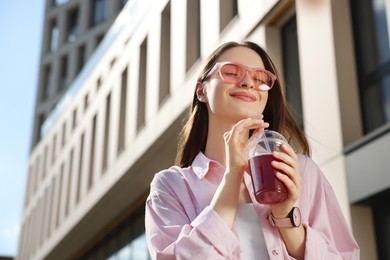 Young woman in sunglasses with plastic cup of fresh juice outdoors, low angle view. Space for text